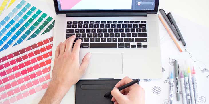 Un diseñador gráfico trabajando en tu tableta y computadora con paletas de colores a un lado de él en el logo de un negocio de diseño gráfico