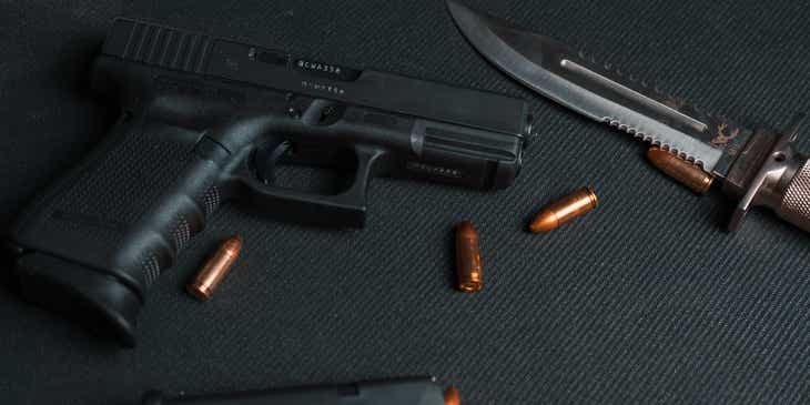 Una pistola, dei proiettili e un coltello sopra il bancone di un negozio di armi da fuoco.