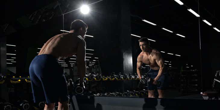 Un uomo che si allena con dei pesi davanti allo specchio in una palestra.