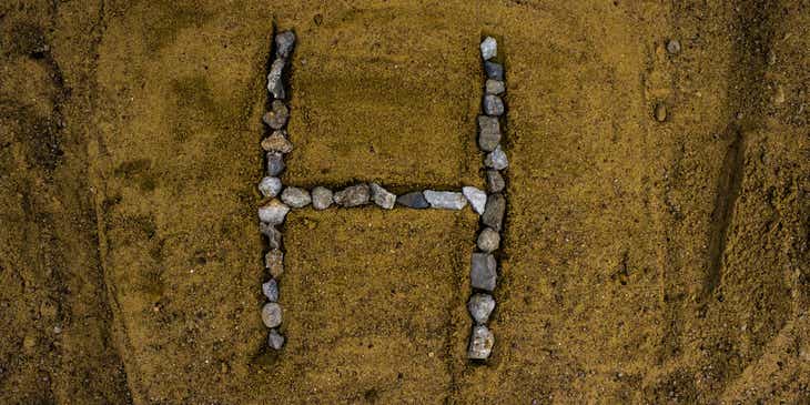 Een letter 'H' gemaakt van steentjes gelegd in zand.
