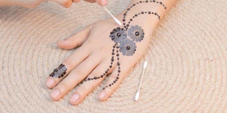Applicazione di henné su una mano con un bastoncino di cotone.