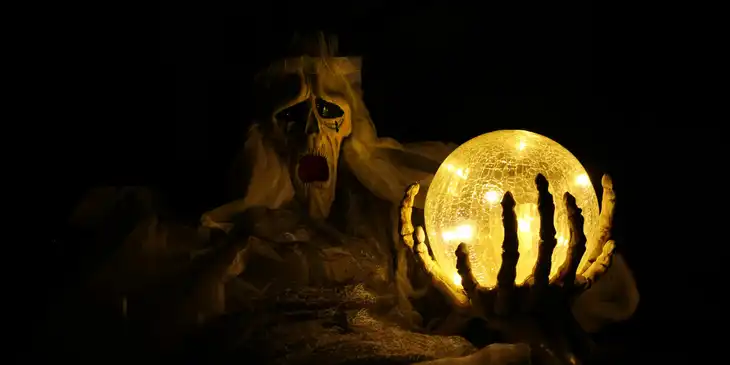 Una fantasmagórica figura de terror sostiene una bola de cristal incandescente sobre un fondo oscuro.