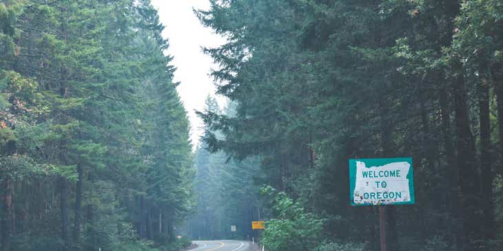 Camino que atraviesa un bosque con un cartel al lado que dice "Bienvenido a Oregón".