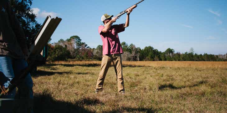 A hunter taking aim with hunting rifle in an open field.