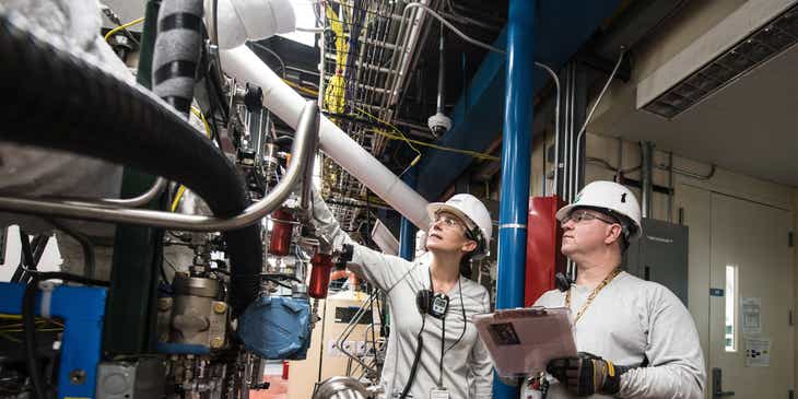 Deux personnes inspectant des machines lourdes dans une installation industrielle.