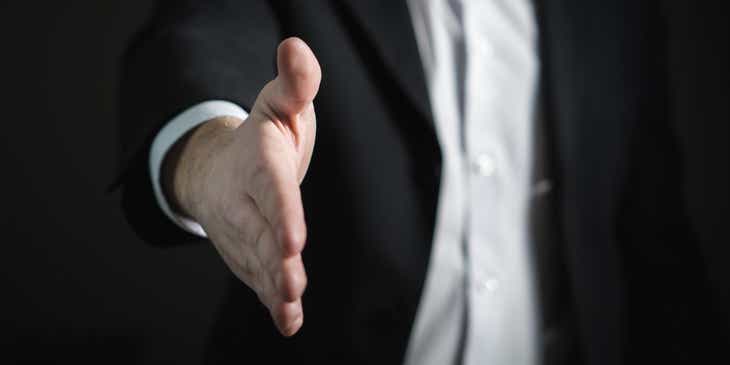 An insurance broker in suit with hand stretched out for a handshake.