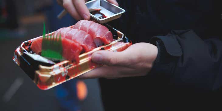 Dłonie trzymające talerzyk z nigiri i sos sojowy w restauracji japońskiej.