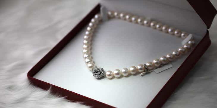 Ein Juwelier stellt eine elegante Perlenkette in einer geöffneten Schachtel zum Verkauf aus.