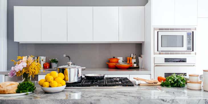 Une cuisine blanche avec une casserole sur la cuisinière et un bol de citrons.