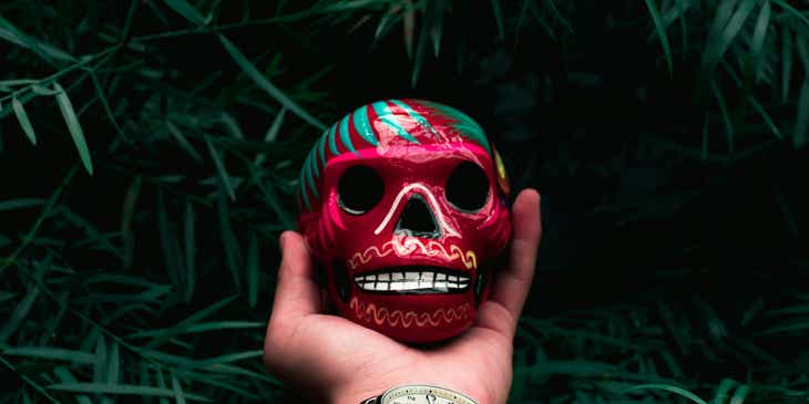 Une main tenant une sculpture de tête de mort colorée.