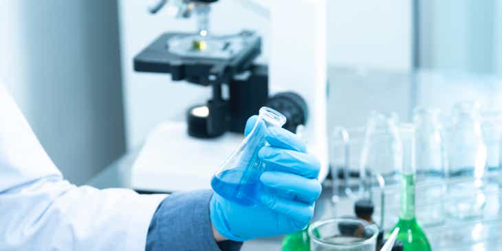 Een medewerker die in een laboratorium een vloeistof in een erlenmeyer bekijkt.