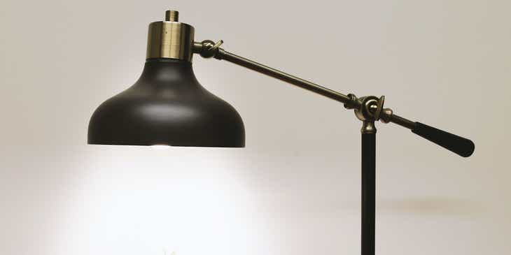 Uma luminária preta em cima de uma mesa iluminando um pequeno vaso de planta.
