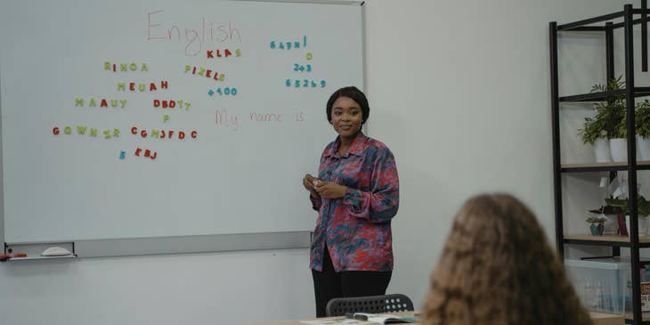 A woman standing in front of a white board teaching English in a language school.