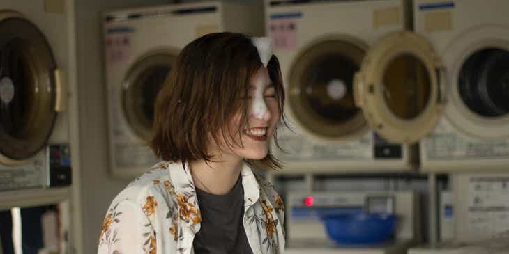 Een lachende vrouw die met zeepsop op haar gezicht haar kleren wast bij een wasserette.