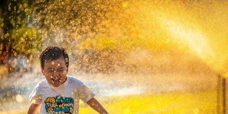 Seorang anak yang bahagia berlari melalui alat penyiram.