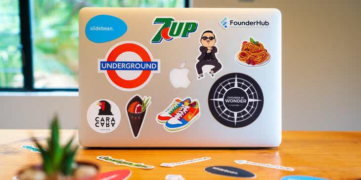 Naklejki z różnymi projektami logo przyklejone do klapy laptopa stojącego na biurku.