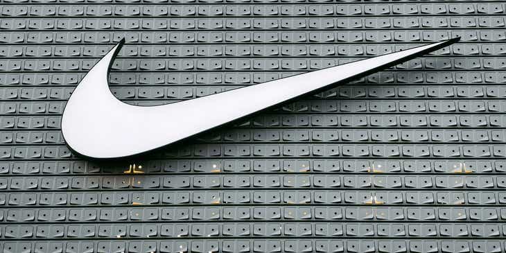 Logo merek Nike berwarna putih yang simple dengan latar belakang abu-abu metalik.