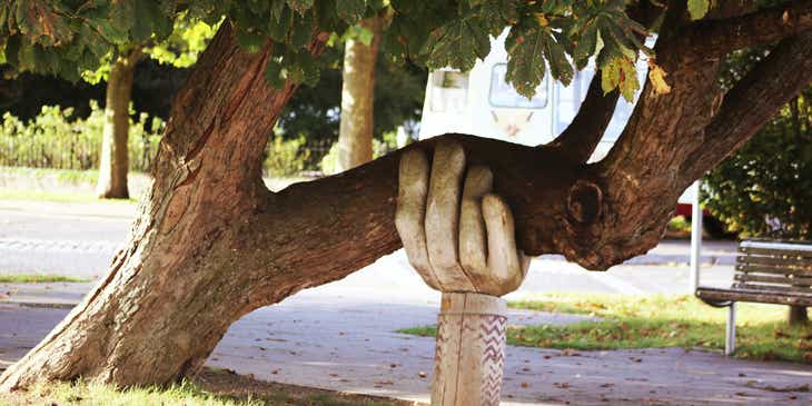 La escultura de una mano debajo de un árbol simulando que lo sostiene, en un logo astuto.