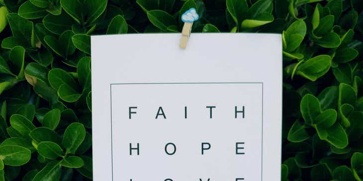 Mano sosteniendo un letrero que dice Faith, Hope, Love, en un negocio basado en la religión