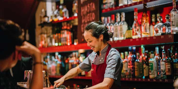 Mujer bartender sonriendo mientras mezcla licores.