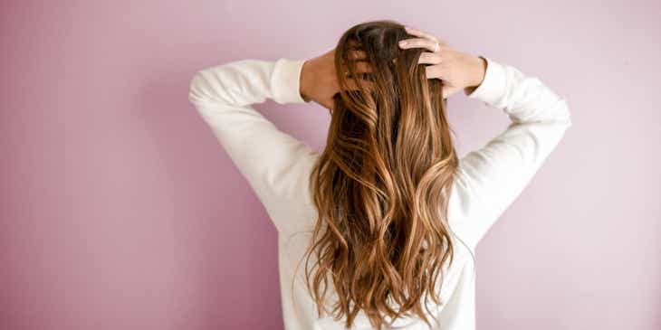 Una mujer parada de espaldas peinando su cabello con las manos.