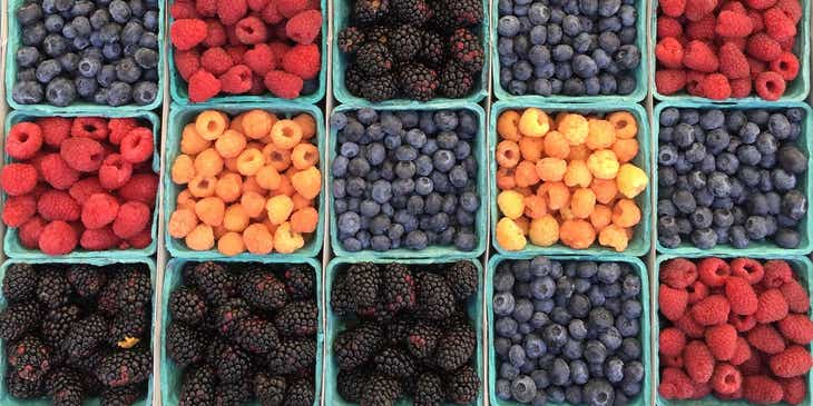 A number of different types of berries, in their respective packaging, at a market.