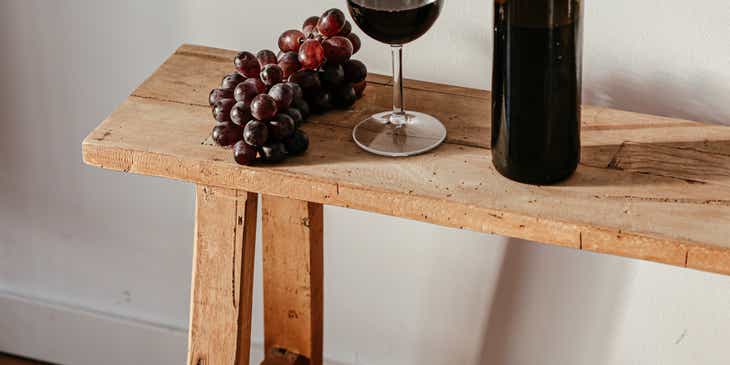 Una botella de vino, una copa y un racimo de uvas sobre una mesa de madera.