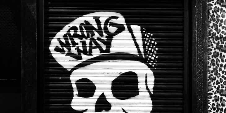 Una calavera punk con una gorra que dice "wrong way" bajo un letrero que dice "Punk Rock" en un portón negro.