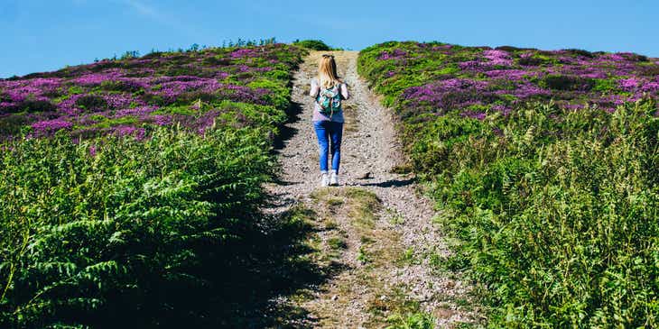 Mujer caminando en un campo rústico con flores moradas.