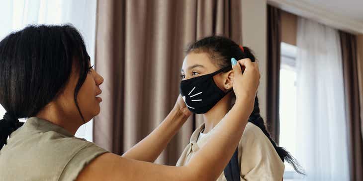 A mother placing a mask on her daughter.