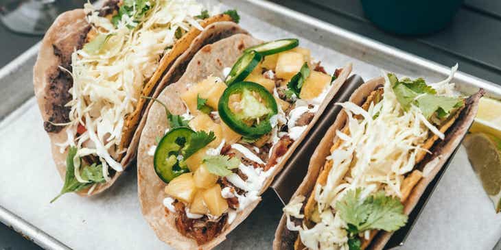 Drei Tacos liegen in einem mexikanischen Restaurant neben Tortilla-Chips auf einem Tisch.
