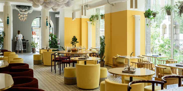 L'interno di un ristorante moderno con mobili e decorazioni in giallo e grandi finestre.