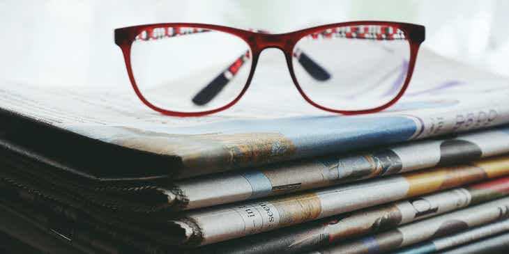 A pair of spectacles resting on a pile of newspapers.