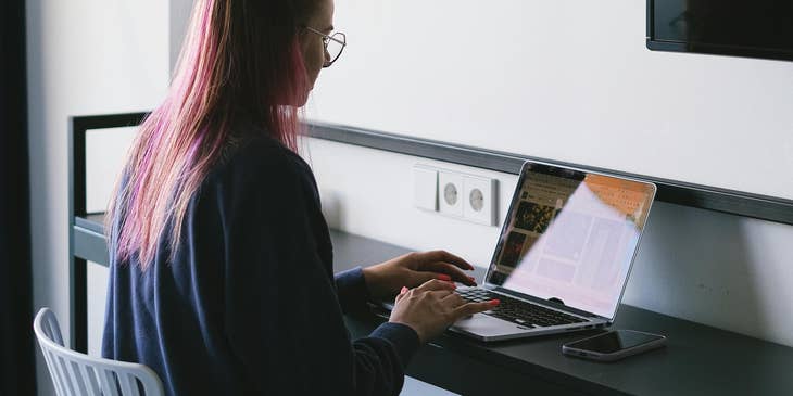 A news journalist working on their laptop at a desk.