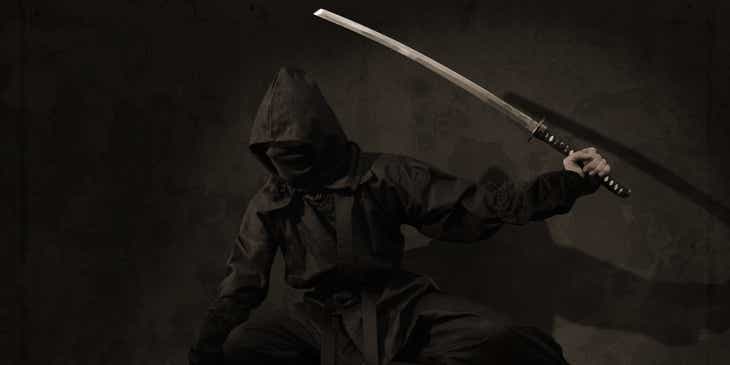 Seorang prajurit ninja berjongkok memegang pedang.