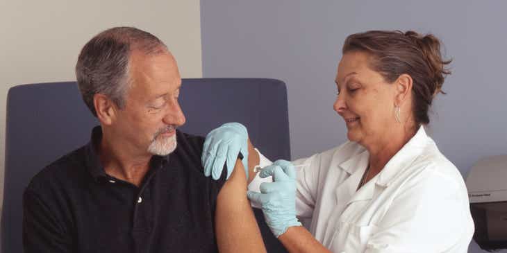 Uma enfermeira injetando uma vacina no braço de um paciente.