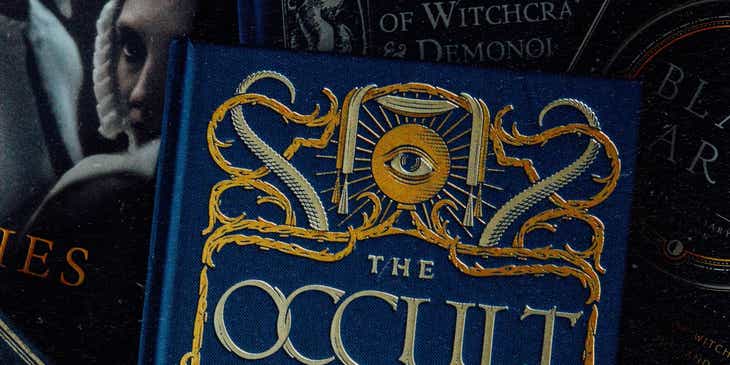 Um livro de ocultismo azul, de capa dura, em um fundo escuro.