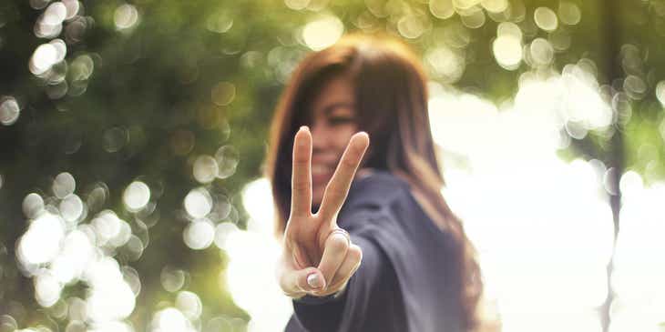 Retrato de una persona sonriendo y mostrando el signo de la paz con las manos en un logo pacífico.
