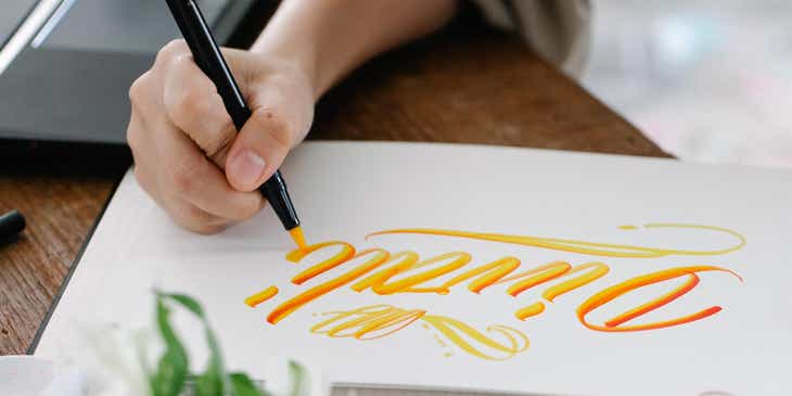 Eine Person entwirft auf einem weißen Kunstblock ein goldenes, persönliches Logo.