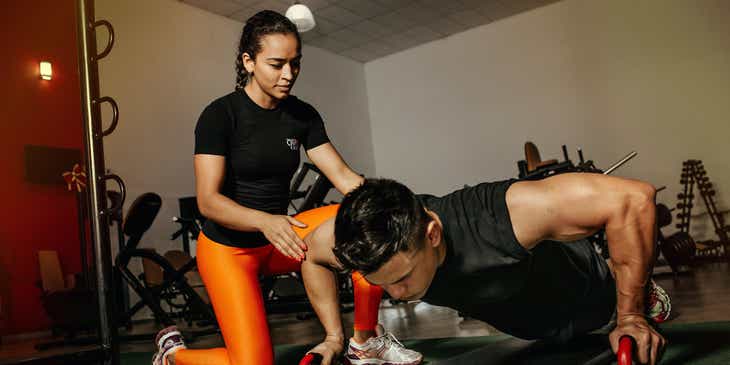 Een personal trainer die de cliënt helpt met push-ups.