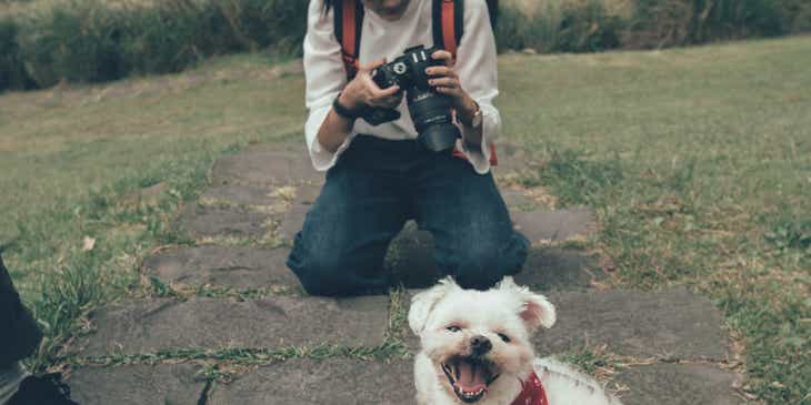 Küçük beyaz köpeğin evcil hayvan fotoğrafını çekmek için kamerasını ayarlayan bir kadın.