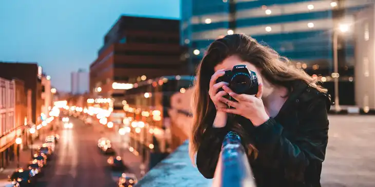 A photographer leaning over a railing by a bridge and taking photos.