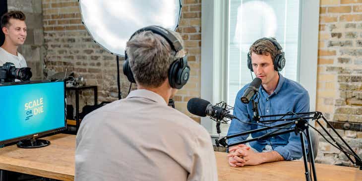 Dua pria berbicara di depan mikrofon di sebuah acara podcast.