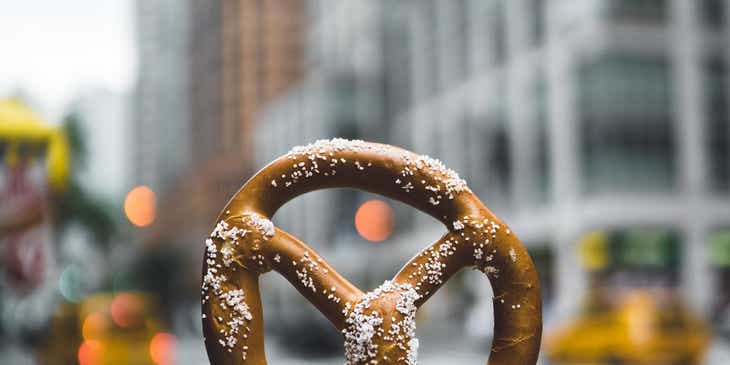 Una mano che tiene un pretzel davanti a uno sfondo urbano.