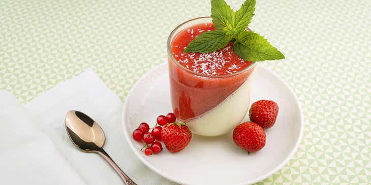 A strawberry and vanilla pudding displayed with a spoon on a white table.