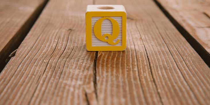 Ein gelbes „Q“ ziert einen Bauklotz, der auf einem grobfaserigen Holztisch liegt.
