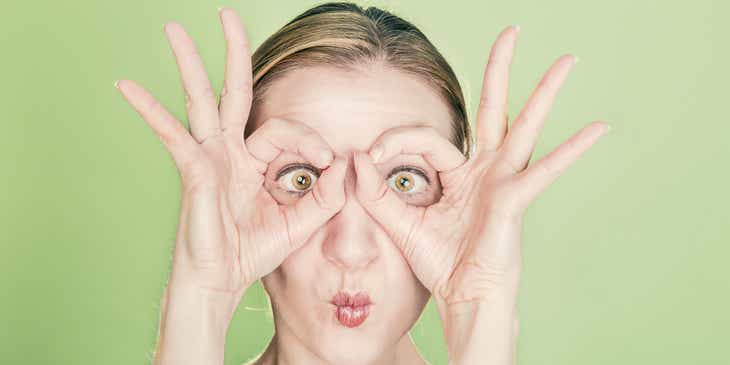 Eine Frau zieht ein Gesicht und formt mit ihren Fingern eine Brille, um einen skurrilen Eindruck zu hinterlassen.