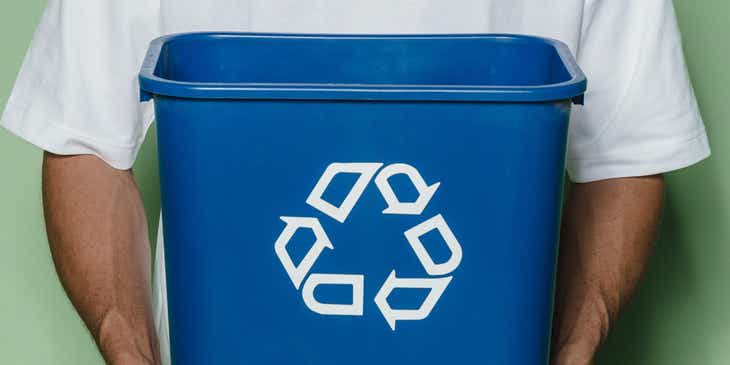 A man holding up a blue recycling bin.