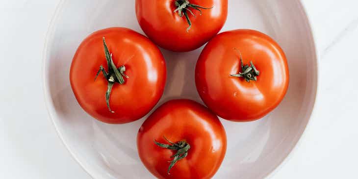 Vier rote Tomaten liegen auf einem runden, weißen Teller.