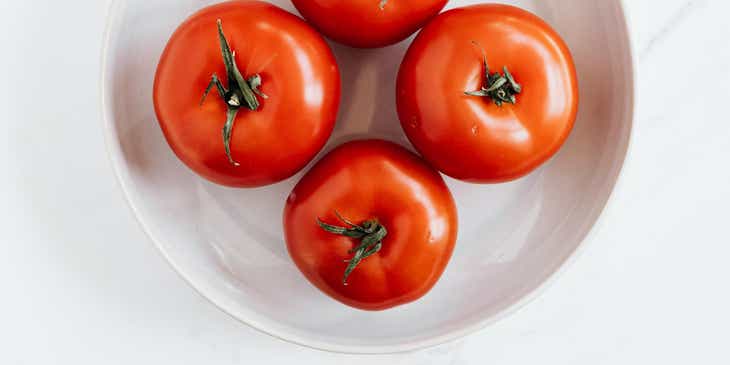 Empat tomat di atas piring putih membentuk lingkaran merah dan putih.